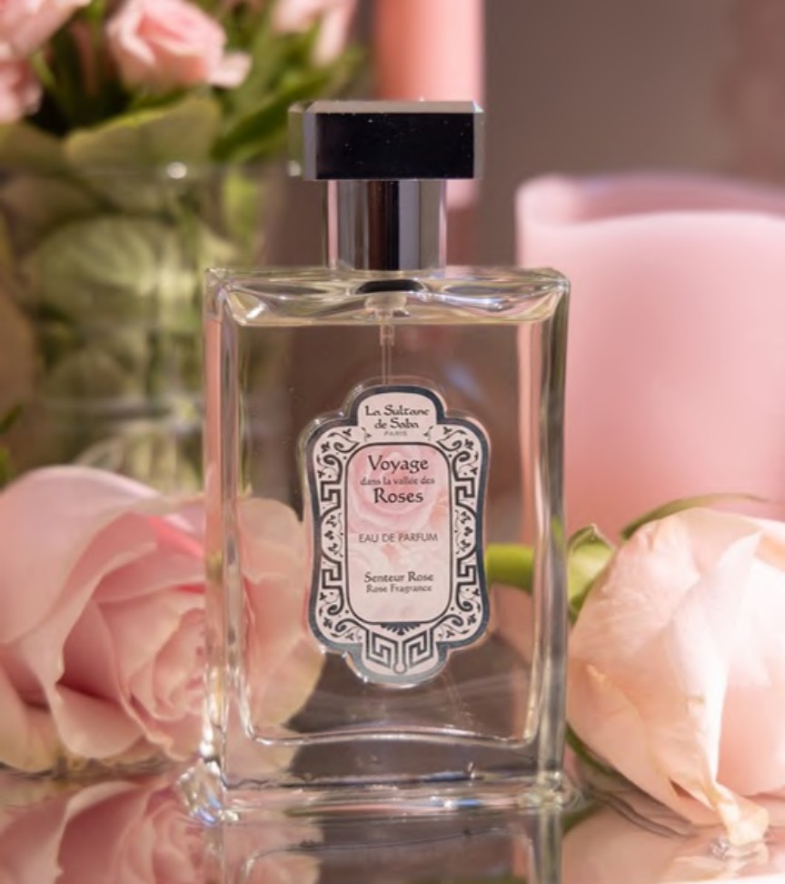 Flacon de l’eau de parfum à la rose présenté parmi des fleurs roses